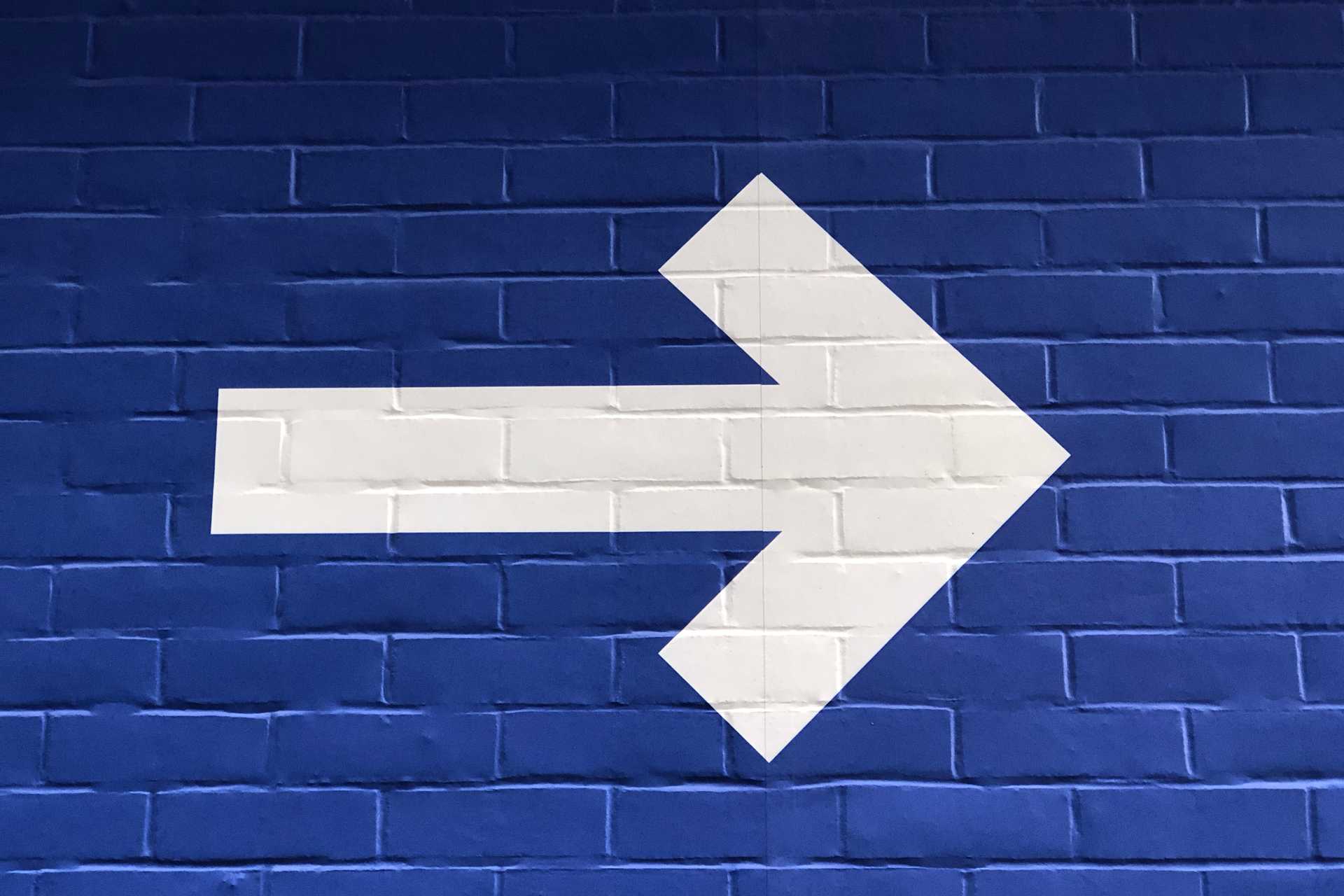 white arrow and blue background painted on bricks showing the onward, the way forward